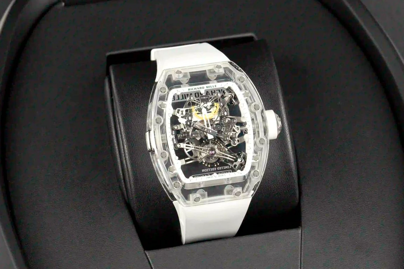 A Richard Mille with a transparent sapphire case and skeletonised tourbillon movement on a white rubber strap, resting in its open black presentation box