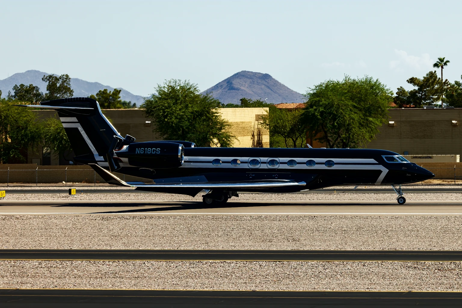 A black and silver Gulfstream G600 rolling out on the runway at Scottsdale, a desert peak behind