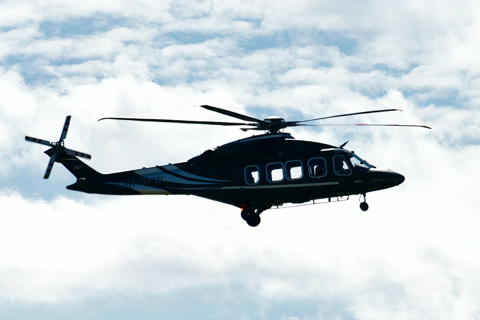 A black twin-engine VIP helicopter in flight against white clouds