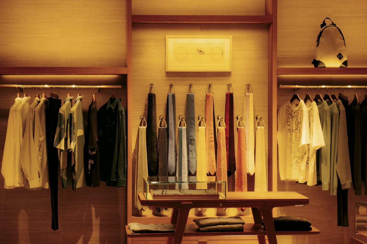 The interior of a luxury menswear boutique, silk ties hung on brass hooks between rails of shirts under warm light