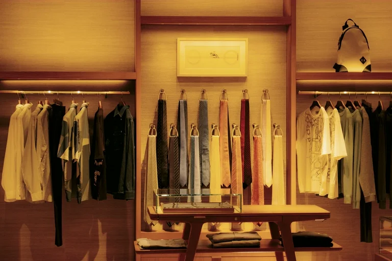 The interior of a luxury menswear boutique, silk ties hung on brass hooks between rails of shirts under warm light