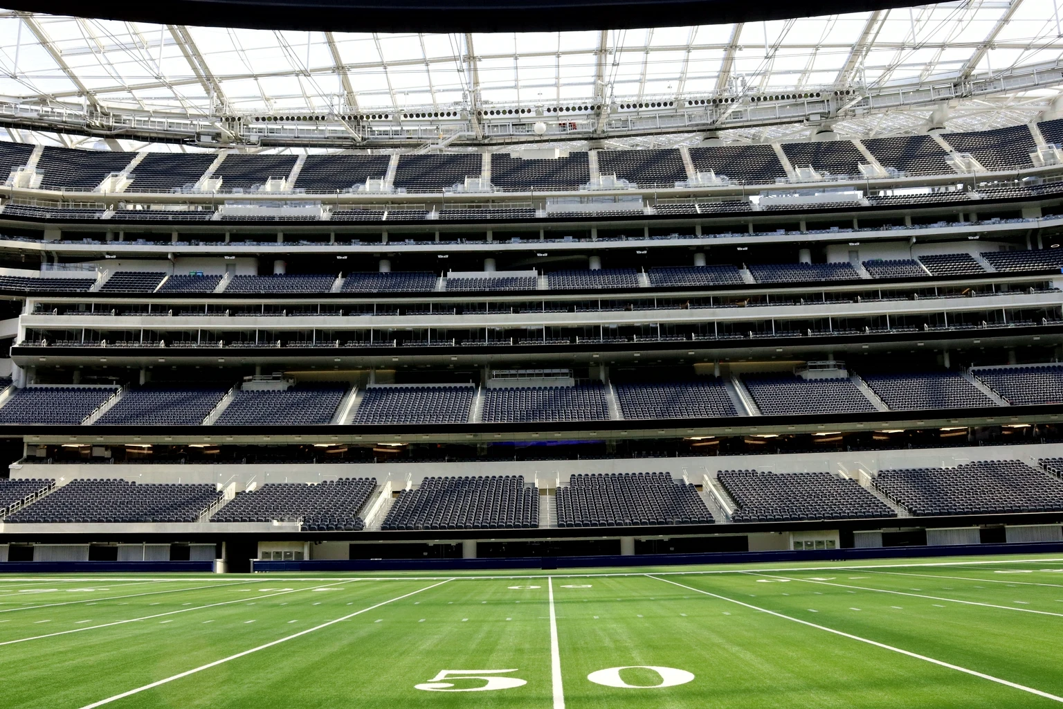 The sideline stands of SoFi Stadium seen from the 50-yard line, with the lower bowl, the field-level clubs behind glass and the suite tiers above
