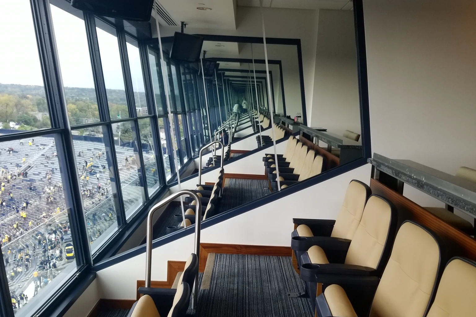 Inside a stadium luxury box: cream leather seats at the glass, the crowd filling the bowl below