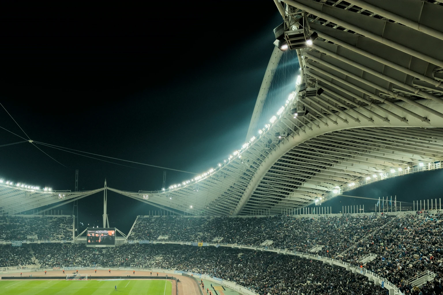 A full stadium at night under a sweeping white roof lit by floodlights