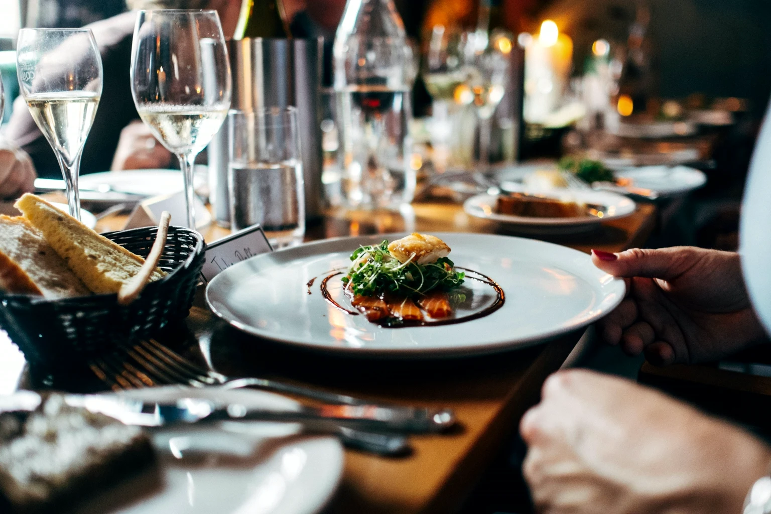 A plate being set down at a candlelit table, champagne glasses in the foreground