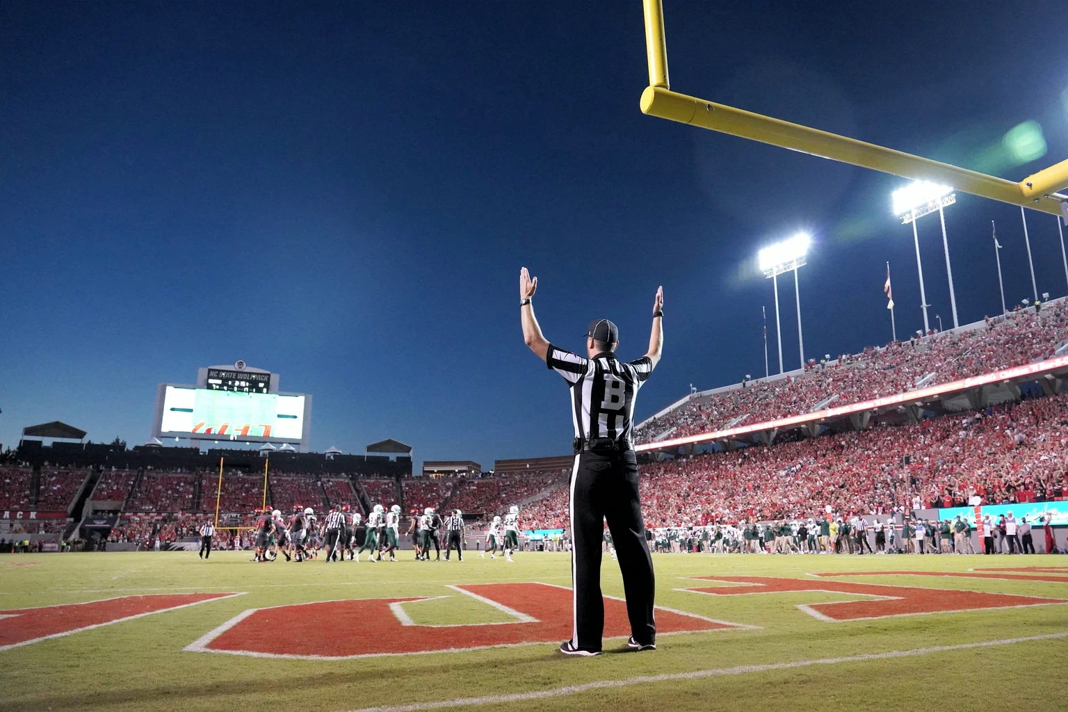 A referee signals a touchdown under the floodlights of a full stadium at night