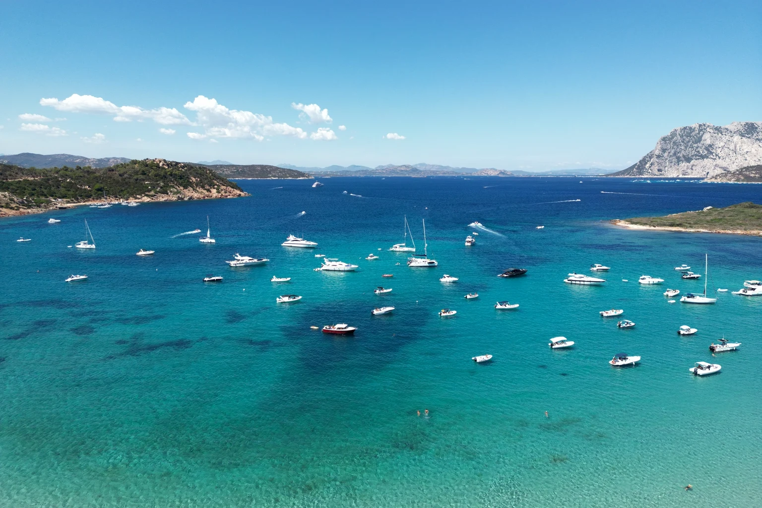 Yachts and motor boats at anchor in a turquoise Mediterranean bay, with a limestone island behind