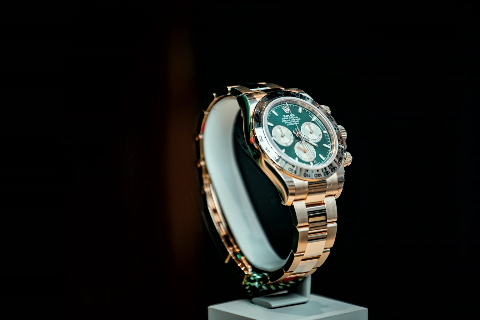 A yellow gold Rolex Cosmograph Daytona with a green dial on a display stand, lit against black