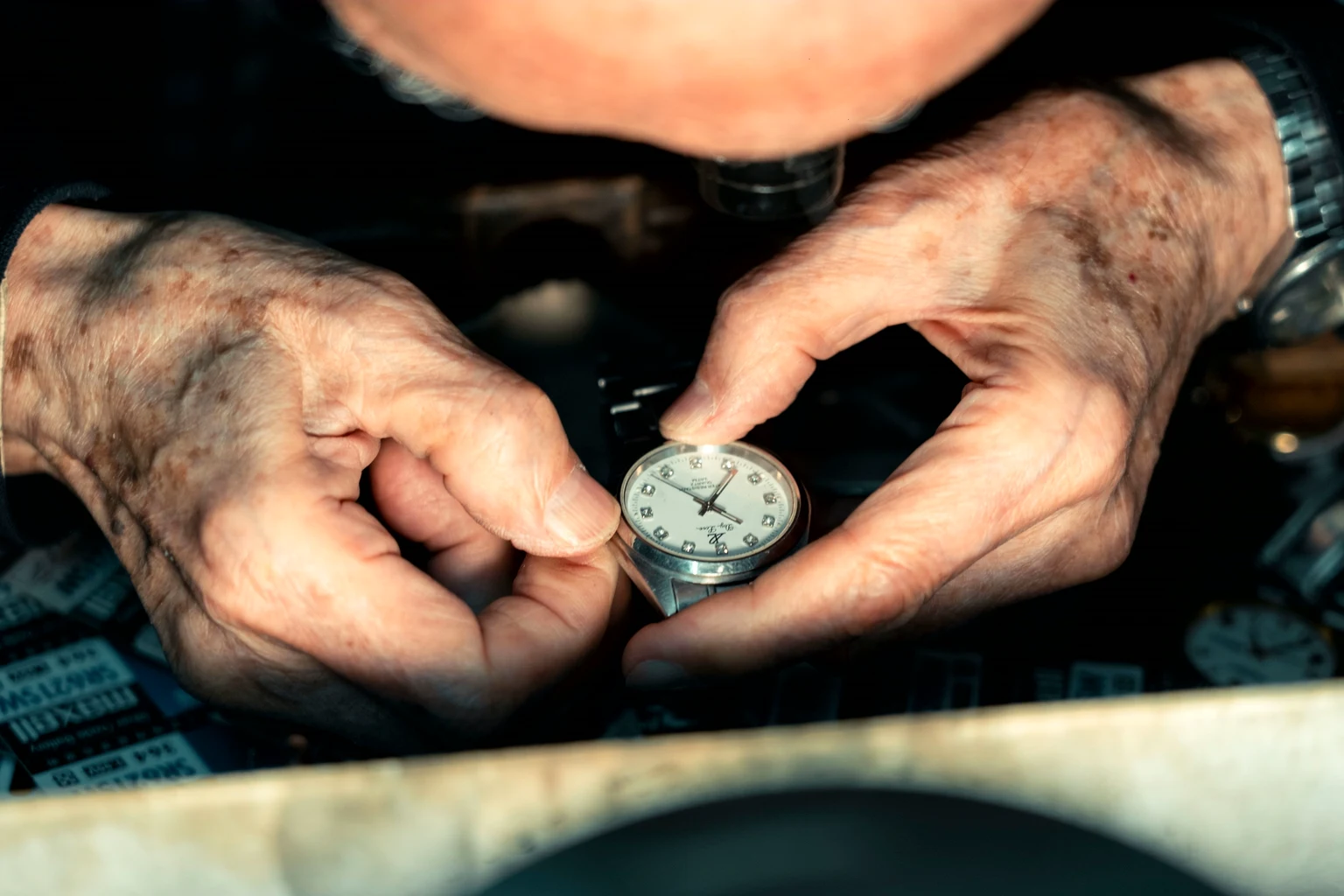 A watchmaker's weathered hands holding a pocket watch at the bench