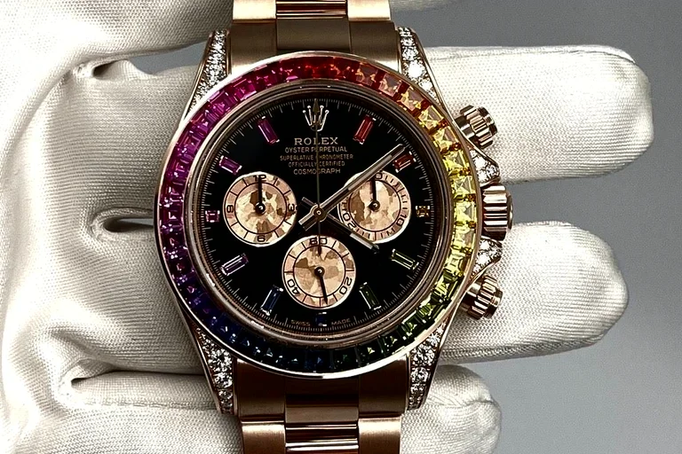 An Everose gold Rolex Cosmograph Daytona Rainbow, its bezel set with graduated coloured sapphires and a black dial, held in a white-gloved hand