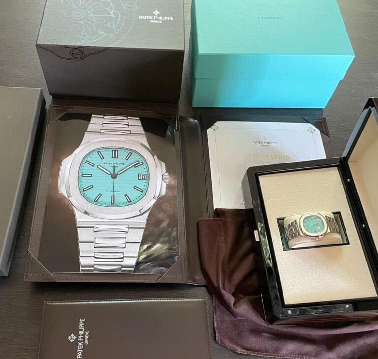 A luxury watch displayed with its box and certificates on a table, surrounded by packaging from other high-end brands.